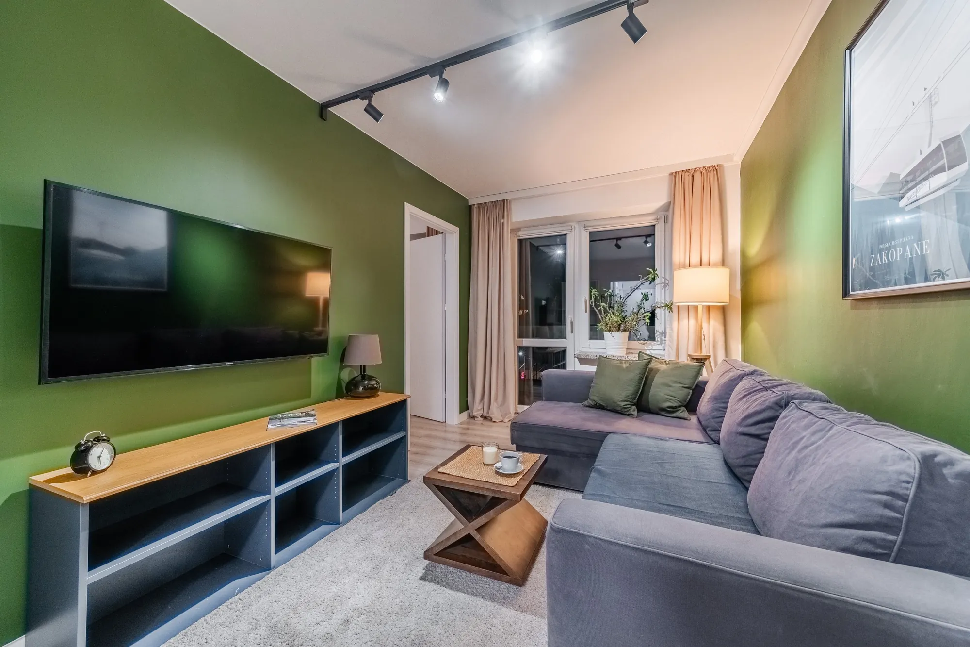 Living room with a green wall, corner sofa and a large TV